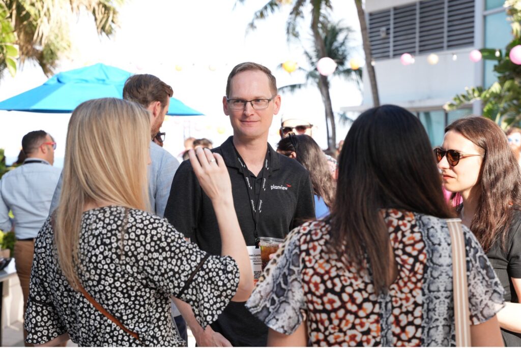 Picture of a man smiling and talking with a group of people | Conference attendees gather at Planview Connect 2025