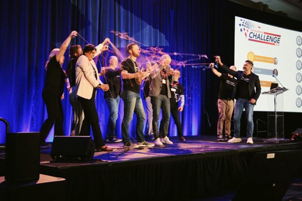 An image of people on a stage spraying each other with silly string as a light-hearted prank.